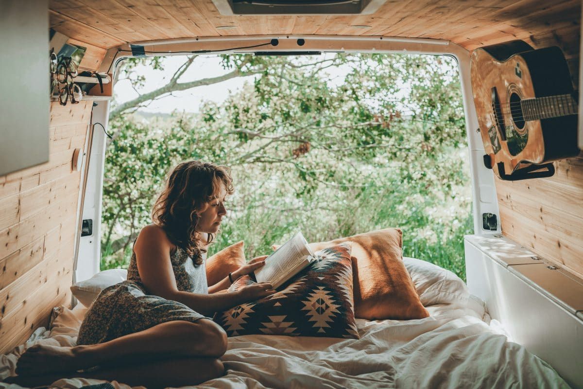 Van life showing a millennial girl reading in her van with nature in the background